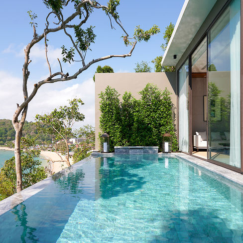 an infinity pool attached to large sliding glass doors in to a hotel room with views of trees and the beaches and ocean waters below