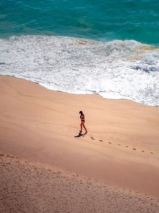 woman walking alone on the beach with footprints imprinted in the sand as the water crashed along the sand