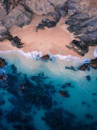 aerial view of a clear blue beach with big rocks