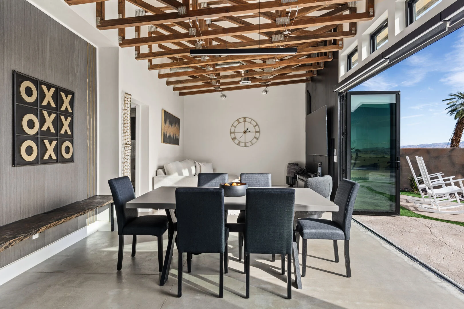 exposed wood beams and joists above a open foorpting with a dining room and living room and large floor to ceiling glass doors open to the outdoors 