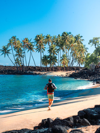 man walking along a white sand beach with turquoise blue water and palm trees standing in the background