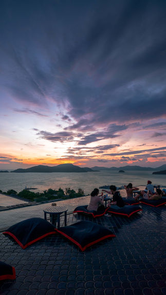 sky exploding with color from a roof top bar in Phuket with cushions and low tables as guests sit and sip cocktails with the view