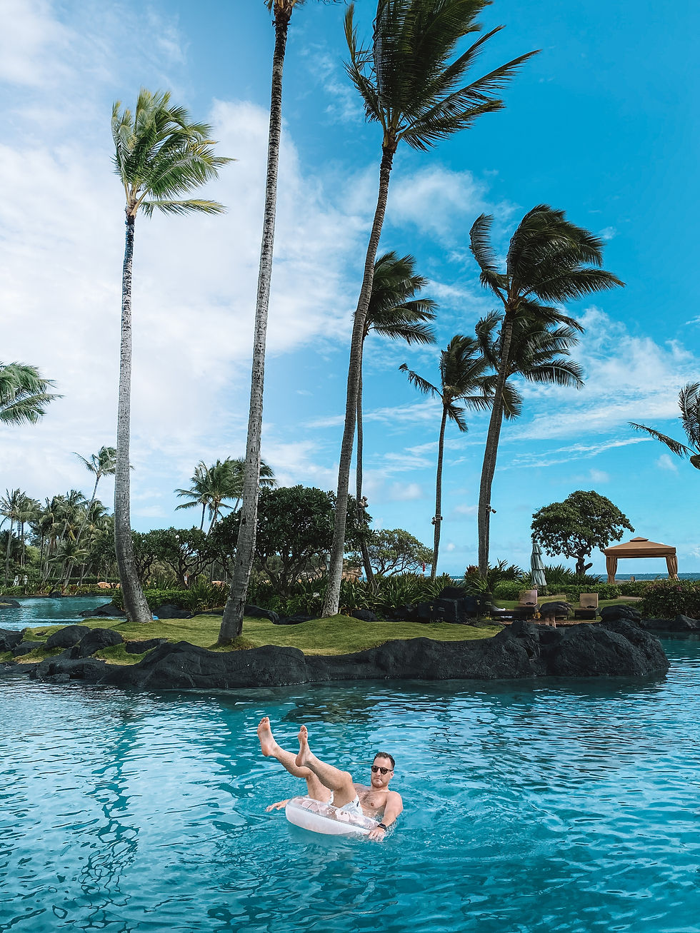 man in a tube raft in the middle of the bright blue water lagoon surrounded by palm trees and black lava rock at grand Hyatt kauai