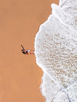 aerial photo of a man and woman couple in the sand as the ocean water touches them