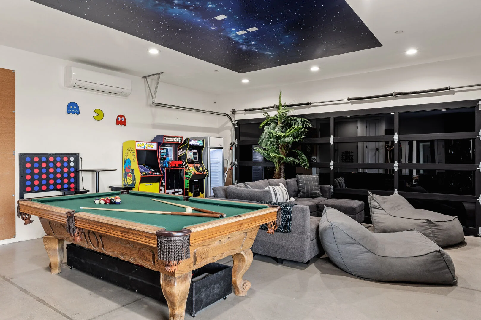 arcade and pool table with large couches and comfortable seating area in a garage 