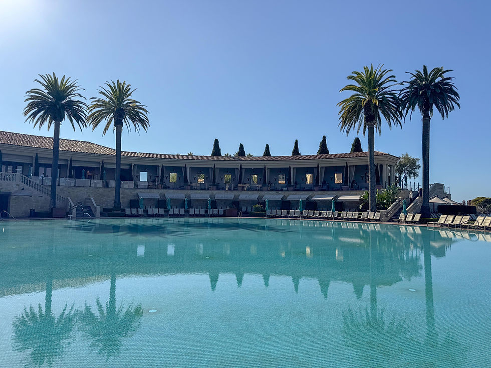 two story building surrounded and overlooking a large pool area with lounge chairs and palm trees with shadows cast in to the water