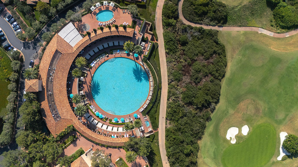aerial view looking down at a massive circular pool surrounded by palm trees and a C shaped building with lounge chairs, cabanas, and seating areas with another smaller pool off to the top and a golf course to the right