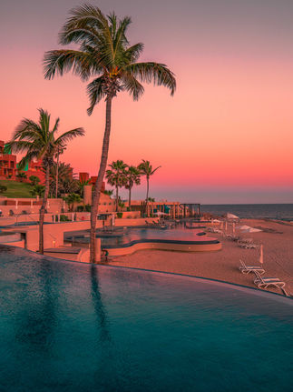 sunset sky over the infinity pools along the sandy beach with palm trees