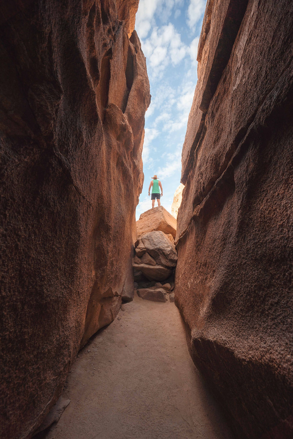 hiker in green shirt standing on the top of a boulder at the end of a slot canyon trailhead in the hall of horrors in Joshua tree national park