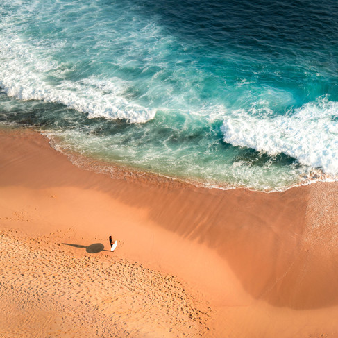 surfer standing on the beach looking out to the water as the shadow casts next to them