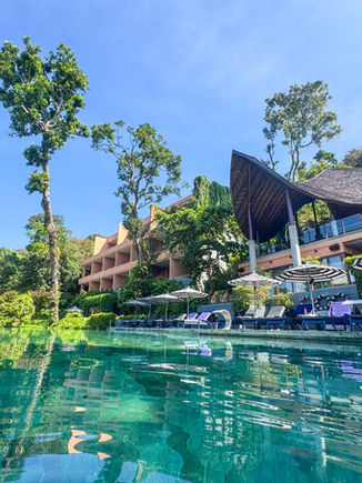 view of the Sri Panwa Habita orange resort from in the pool waters next to lounge chairs and umbrellas
