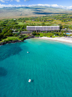 Mauna Kea iconic resort tower standing along the white sand beaches against tropical blue ocean waters and lush green landscaping on the Big Island of Hawaii