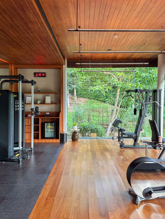 black gym equipment with cardio equipment on top of wood floors surrounded by large floor to ceiling glass windows looking at vegetation outside and covered with a wood plank ceiling
