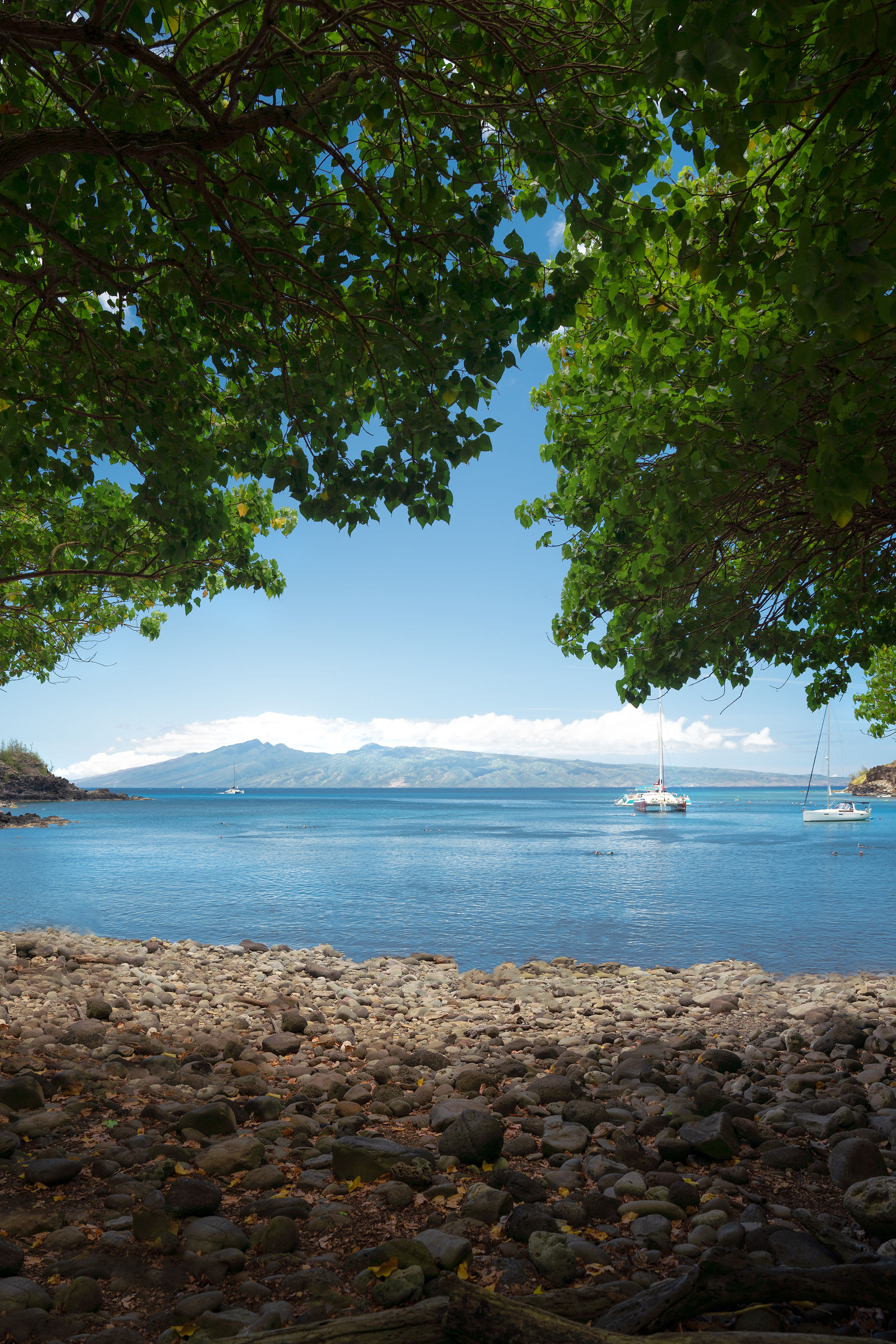 beach and Hawaii island ocean water with catamaran boats and rocky beach 