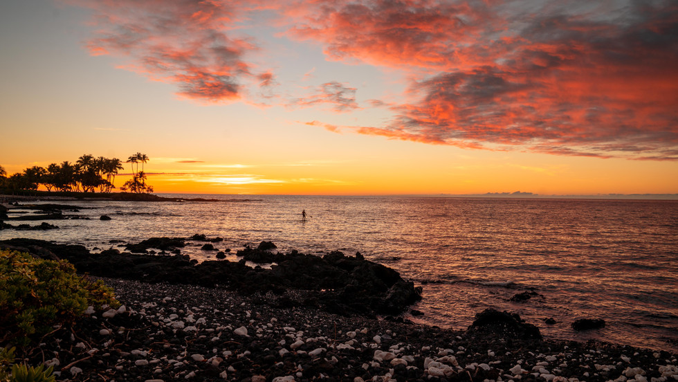 sunset filled sky with red clouds as a man in a paddle board stands on the water as a silhouette in the distance