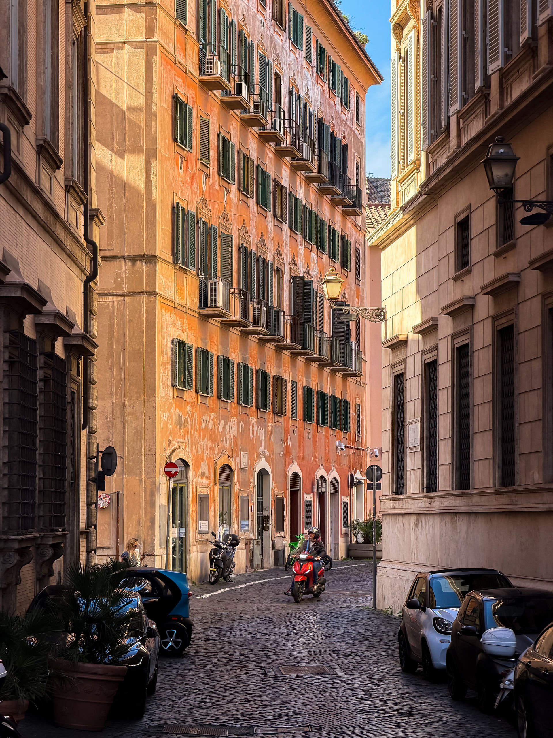 red vespa driving down a quiet road in Rome 