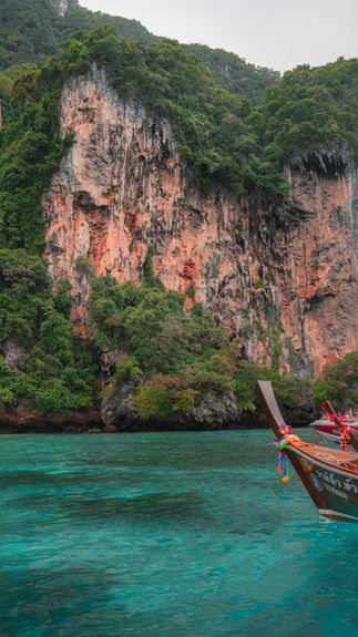 long tail boat sitting in vibrant blue waters in front of orange rocky cliffs covered in lush green vegetation