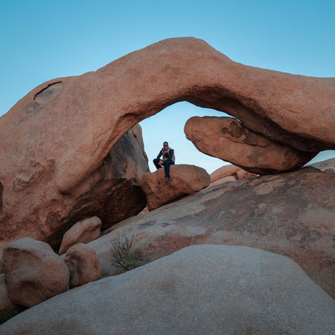 man sitting on top of a rock underneath a large arched rock formation