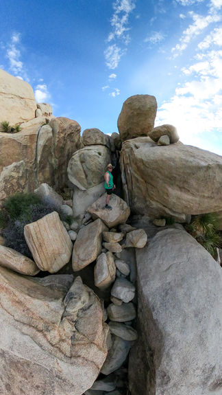man standing on top of a pile of rocks in front of a hidden and dark slot canyon