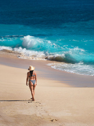 woman in bikini walking along the beach and vibrant blue waters in cabo