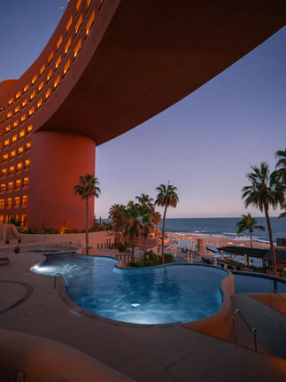 nighttime views of the pools illuminated at night surrounded by palm trees and the cantilevered structure