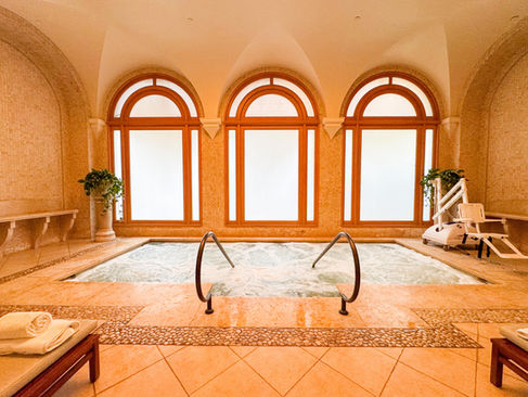 3 large floor to ceiling windows with arches above in a large vaulted ceiling with a hot tub in the middle