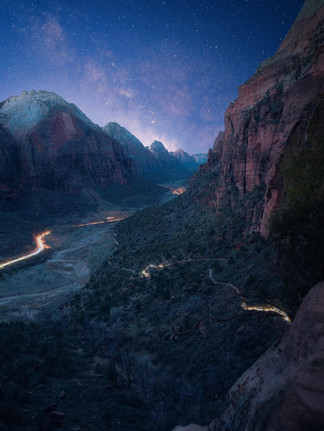 light trails illuminating the valley floor and hiking trails at the Zion national park valley floor as the Milky Way stars and galaxy illuminate the sky over the red rock mountains 