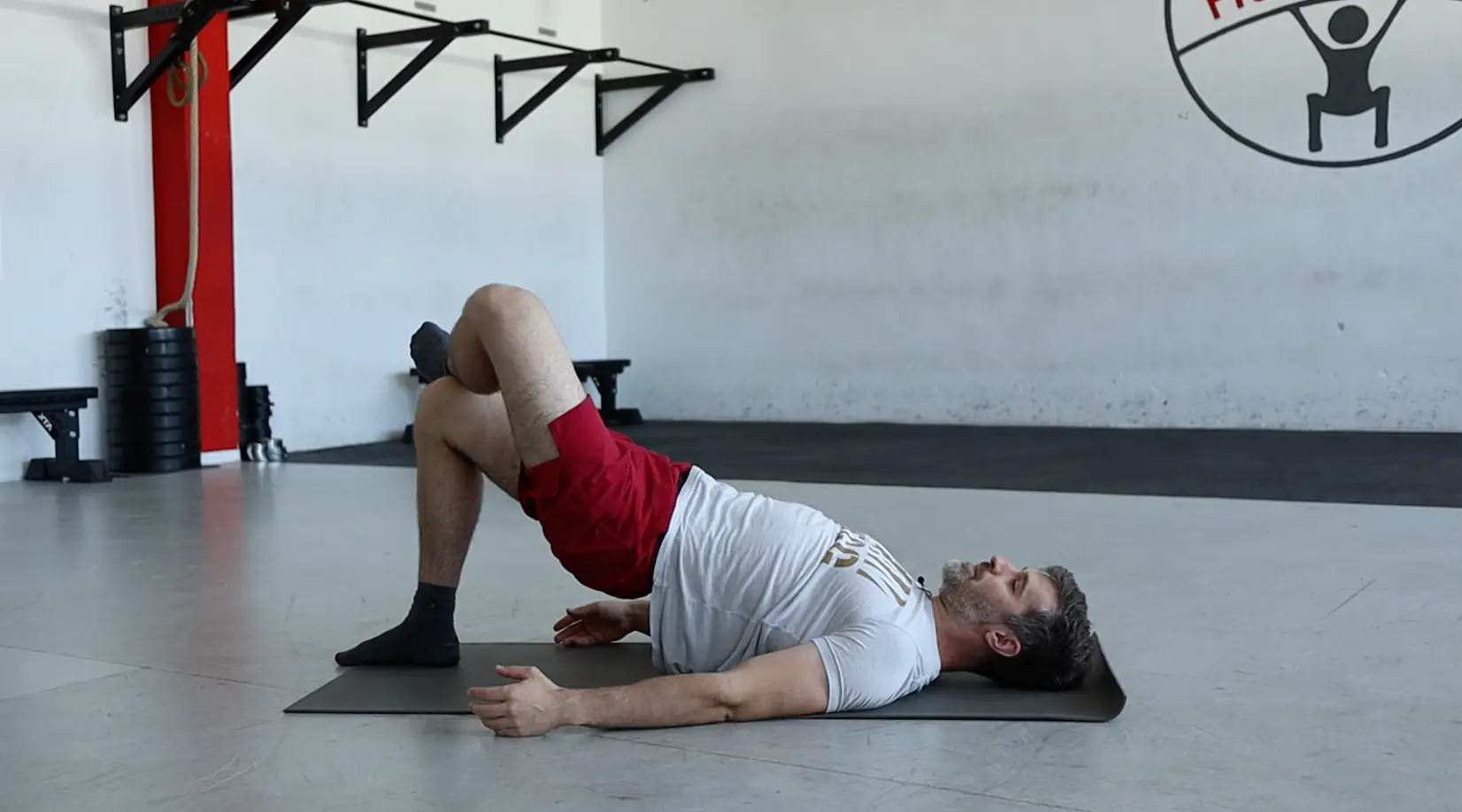 Matteo, Physiotherapeut, macht eine Brücke als Übungen in einer Turnhalle