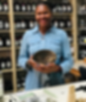 A picture of Nitika, founder of True Grit Life, standing inside of an apothecary holding a bowl of medicinal herbs used to make a remedy.