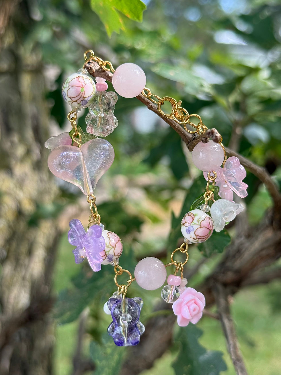 Pink and purple beaded charm bracelet hanging on a branch