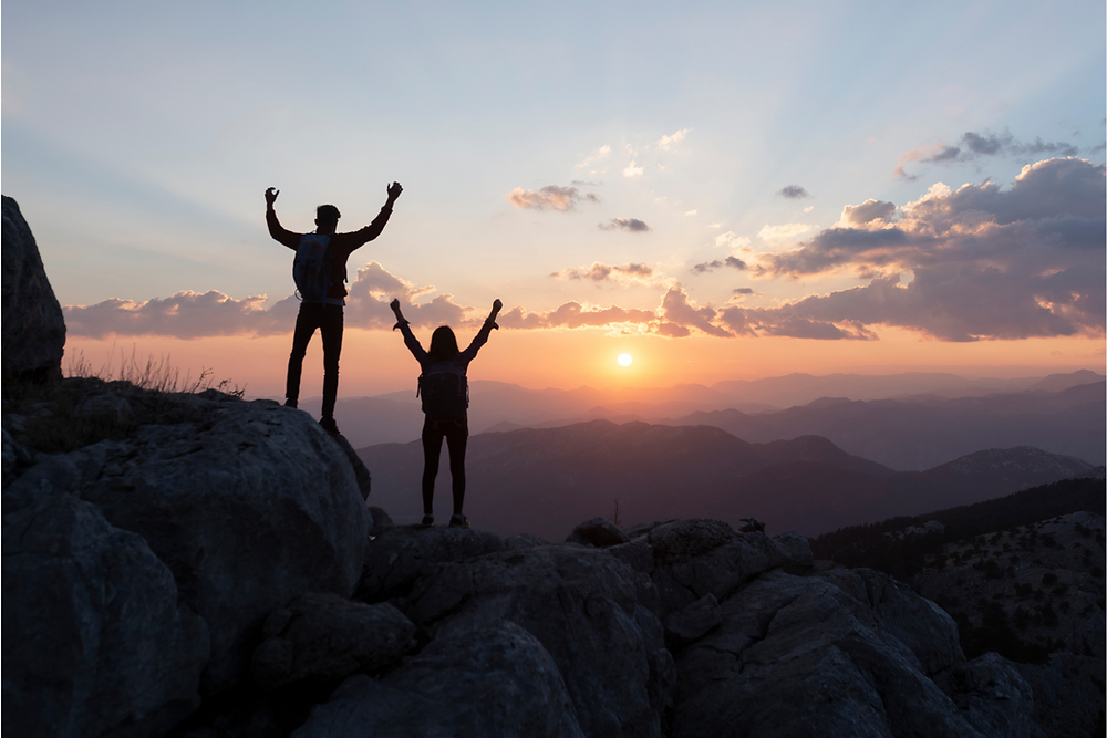 Two people standing on top of a mountain with fists raised in triumph.