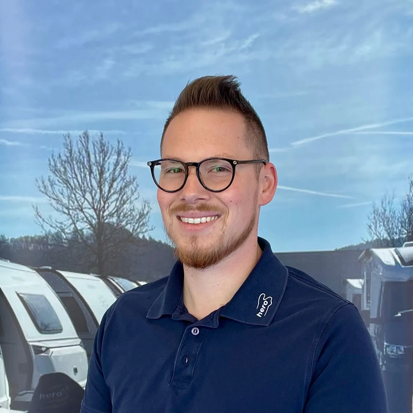 Lächelnder Mitarbeiter mit Brille vor Wohnwagen