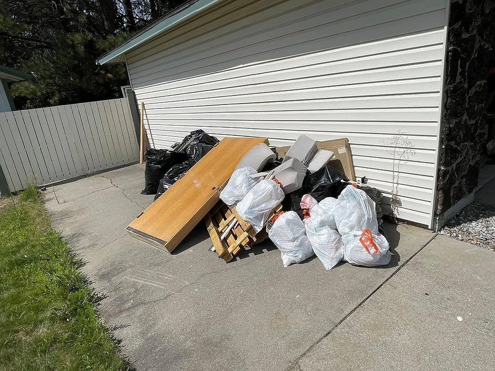 a large pile of junk outside someones home in their driveway including an old door frame, garbage bags, pallets, and old plastic chairs