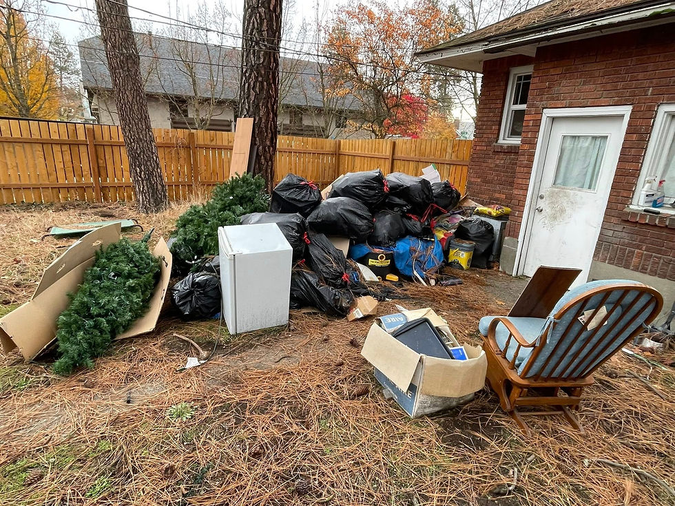 A large pile of collected junk in the back yard of a customers house in the fall time including a mini fridge, boxes, furniture, chairs, garbage bags, and old christmas decorations