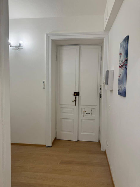 Luminoso corridoio con porta bianca chiusa e pavimento in parquet chiaro.