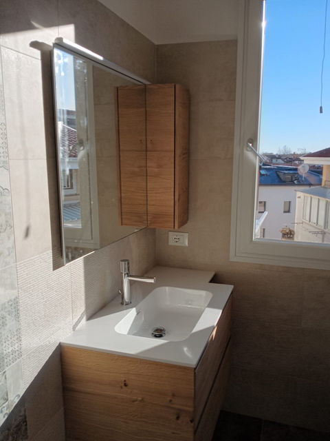 Bagno moderno con lavabo, mobile in legno, finestra luminosa.