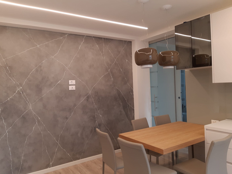 Sala da pranzo moderna con tavolo, sedie e parete effetto marmo grigio.