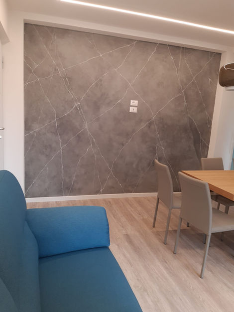 Soggiorno moderno con divano blu, parete grigia, pavimento chiaro e tavolo.