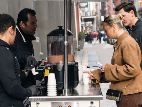 Barista serving hot chocolate from a Sweet Wheels cart at a holiday event in New York City