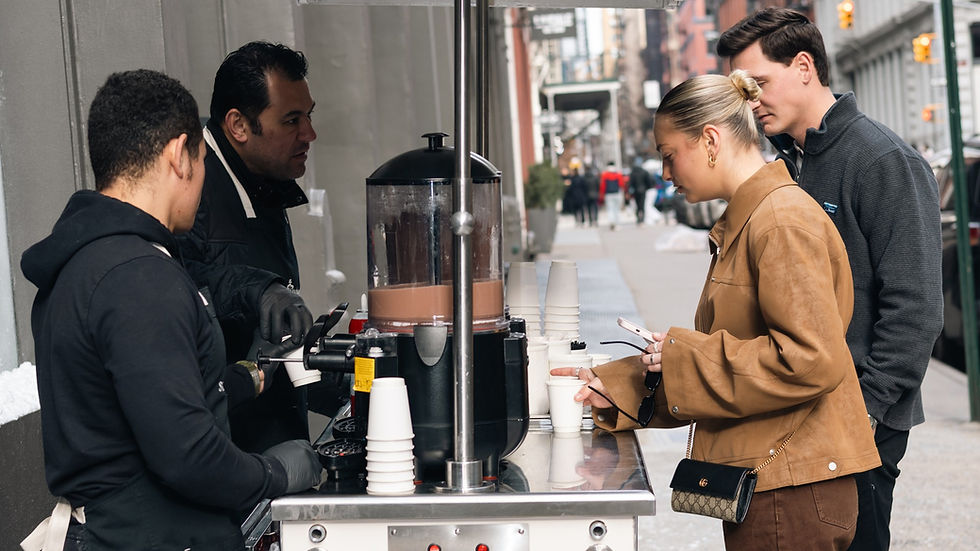 Barista serving hot chocolate from a Sweet Wheels cart at a holiday event in New York City