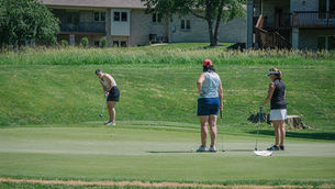 One woman putts while two others watch at a charity golf tournament.