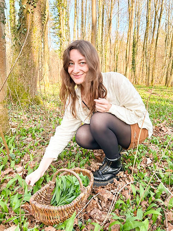 Michelle hockt in einem Bärlauchfeld im Wald und plückt Bärlauch. Vor ihr steht ein Weidenkorb indem sie Bärlauch sammelt.