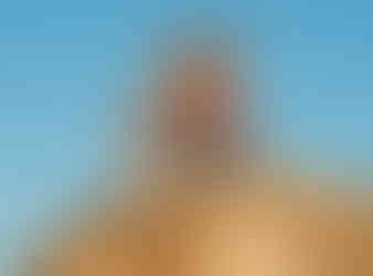 A group of friends and a child posing playfully on top of a large desert rock formation under a clear blue sky.