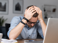 A man sitting at his desk with his face in his hands thinking about a mistake he made.