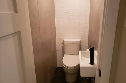 Modern Powder Room with Wall-Mounted Sink, Toilet, Tiled Walls, and Black Flooring by Good Choice Contracting.