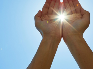 Hands cupped against a clear blue sky, holding sunlight. Bright sunbeams shine through fingers, evoking a serene, hopeful mood.