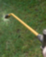 Close-up of a yellow spray nozzle watering grass, creating a fine mist. The background is a lush green lawn, evoking a sense of freshness.