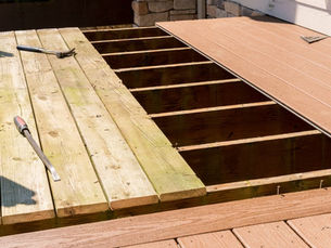 Wooden deck under construction with old and new planks, visible tools, and a partially exposed frame. Sunny day with neutral colors.