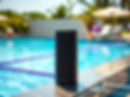 Black portable speaker on pool deck, clear blue water, resort background.