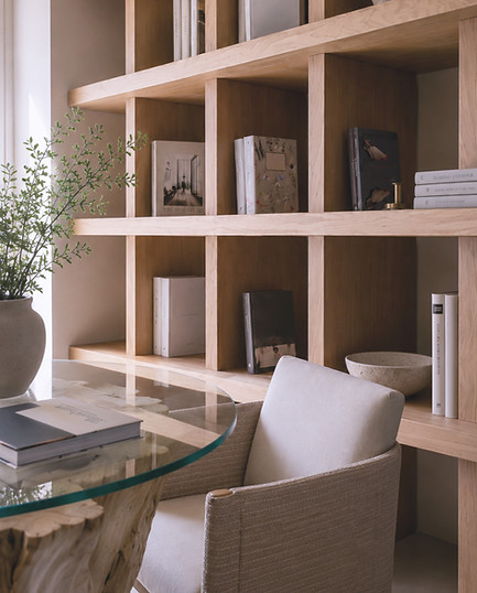 Warm modern custom oak shelving, curated décor, and neutral upholstered chairs